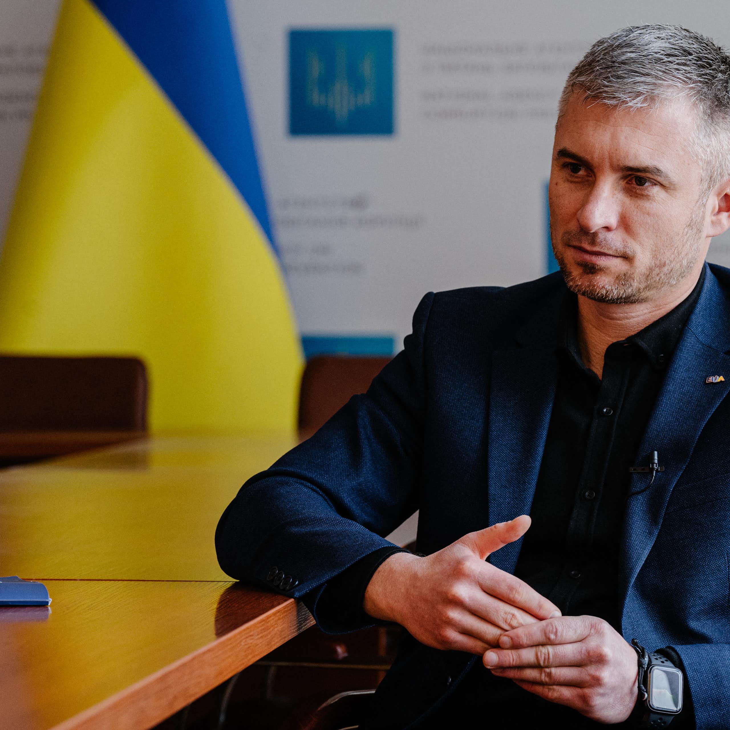 Un homme assis à un bureau, avec le drapeau ukrainien en arrière-fond