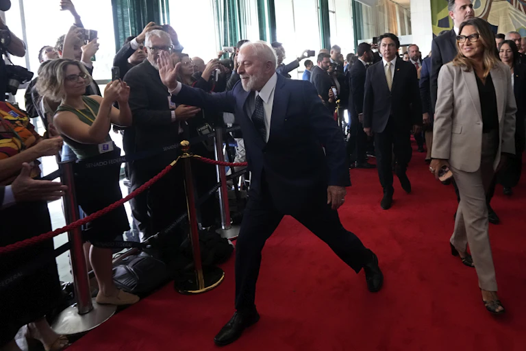 A man with white hair and beard in a suit and tie high fives members of the media while walking down a red carpet.