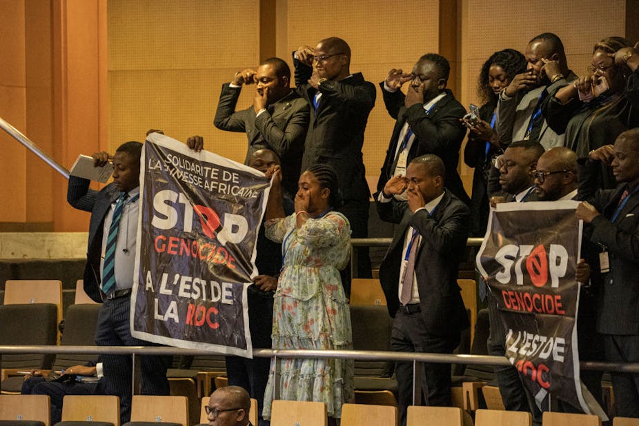 Men in suits and some women hold up banners and raise hands to their faces