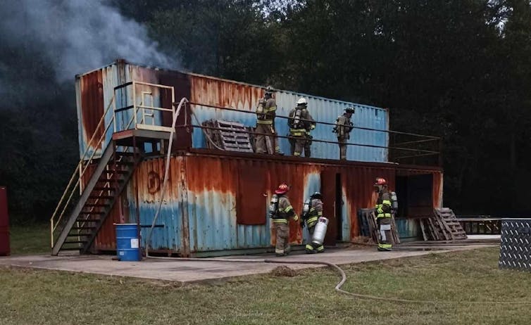 Firefighters practice on a stack of two smoking cargo crates.