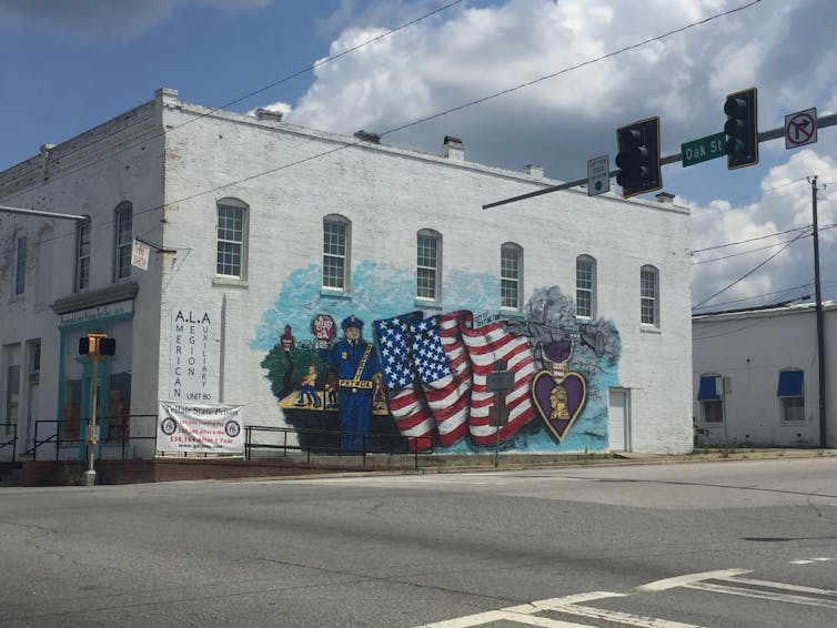 A building with a mural of emergency responders and a US flag. A banner advertises for correction officer jobs at the nearby prison.