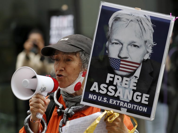 A protestor with a megaphone holds a 'free Assange' sign