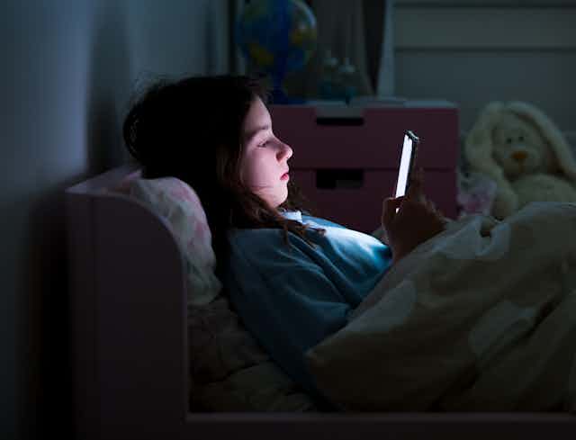 A young teen girl late at night in bed looking at smartphone