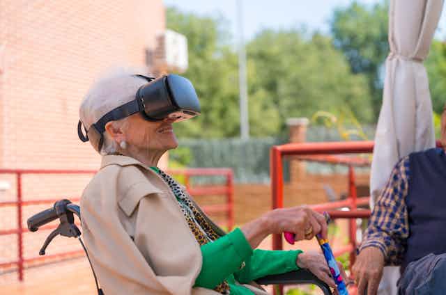 An older woman in a wheelchair uses a VR headset.