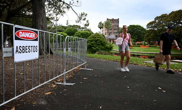 Woman walks past asbestos warning sign in Sydney