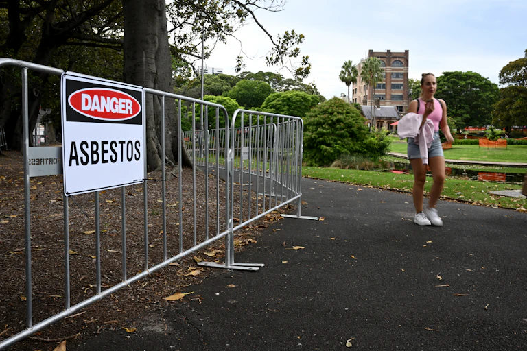 Woman walks past asbestos warning sign in Sydney