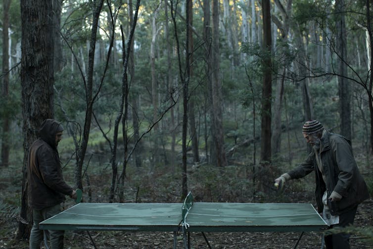 Two men play ping-pong in the woods.