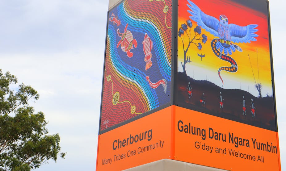 A sign in Cherbourg saying 'many tribes one community' featuring Indigenous artwork.