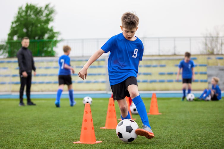 A boy plays kicks a soccer ball between cones.
