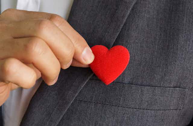 Homme d'affaires agrafant un pin's en forme de coeur sur sa veste.