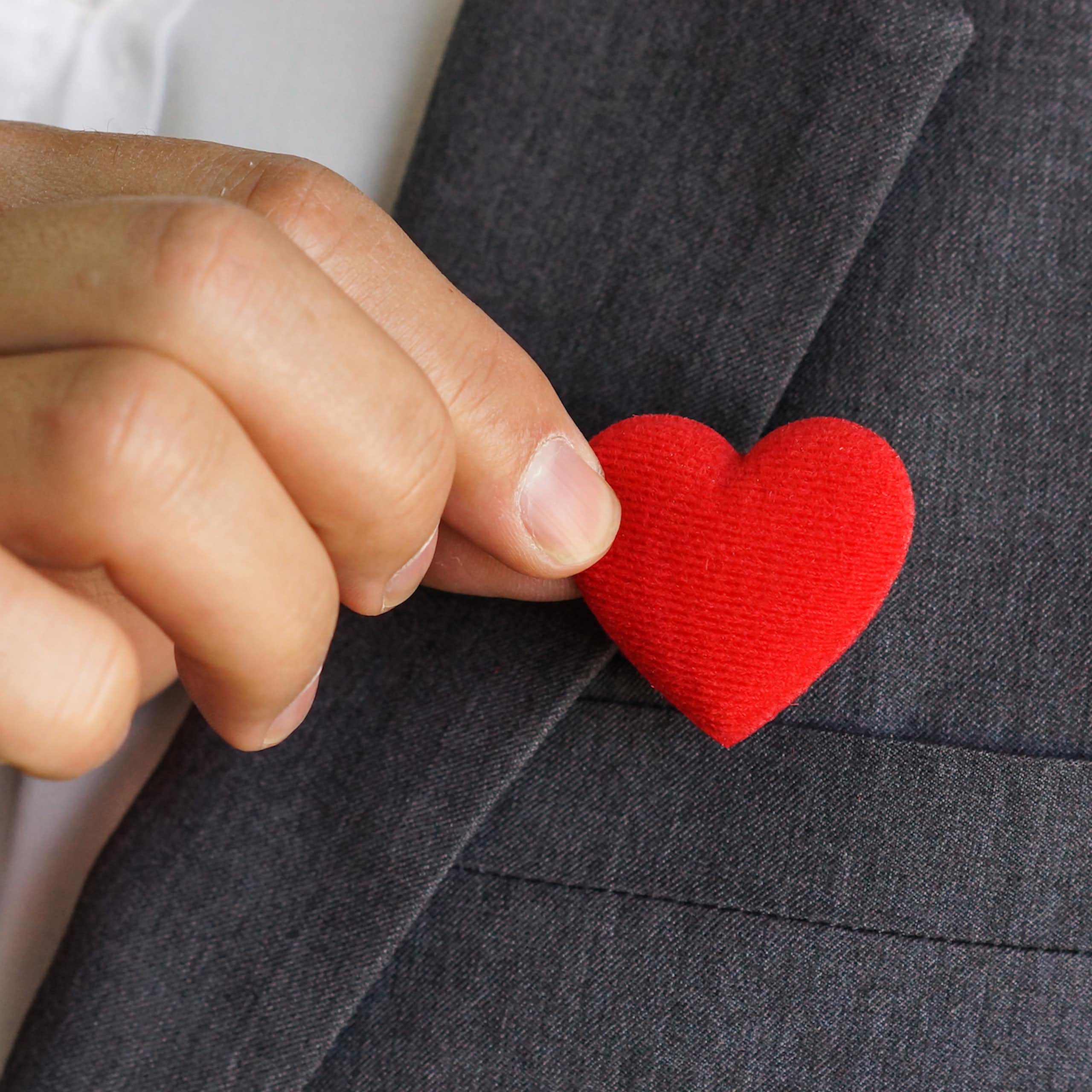 Homme d'affaires agrafant un pin's en forme de coeur sur sa veste.