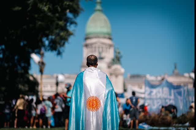 A person, wearing Argentina’s flag, standing in front of a government building during a general strike.