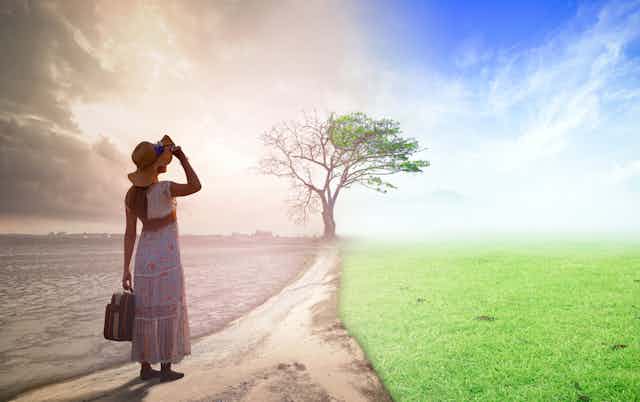 Woman in summer dress with hat and suitcase in foreground, path ahead and background spliut into left side grey barren field and right side green lush field with tree