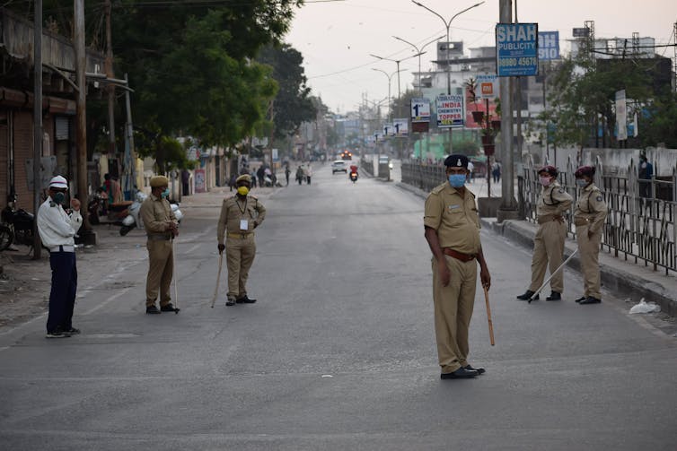 Six Indian police officers wearing masks and standing on a city street.