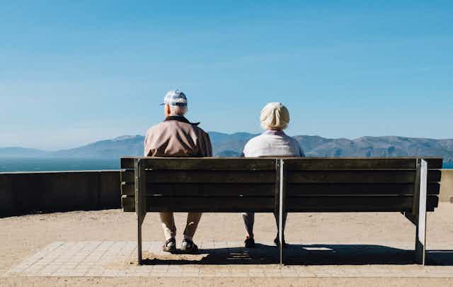 homem e mulher idosos sentam lado a lado em um banco de praça