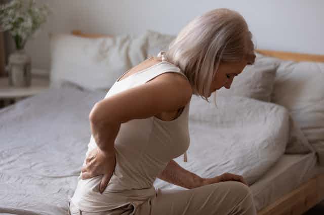 Woman sits on bed, holding her lower back