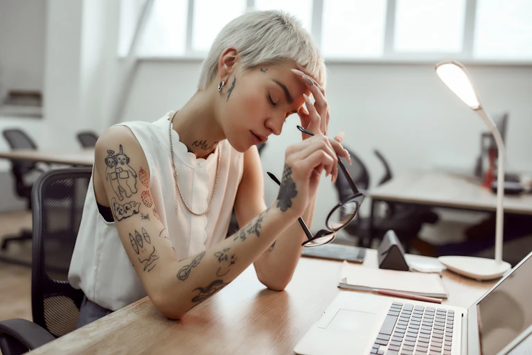 Woman in pain at her desk takes off her glasses