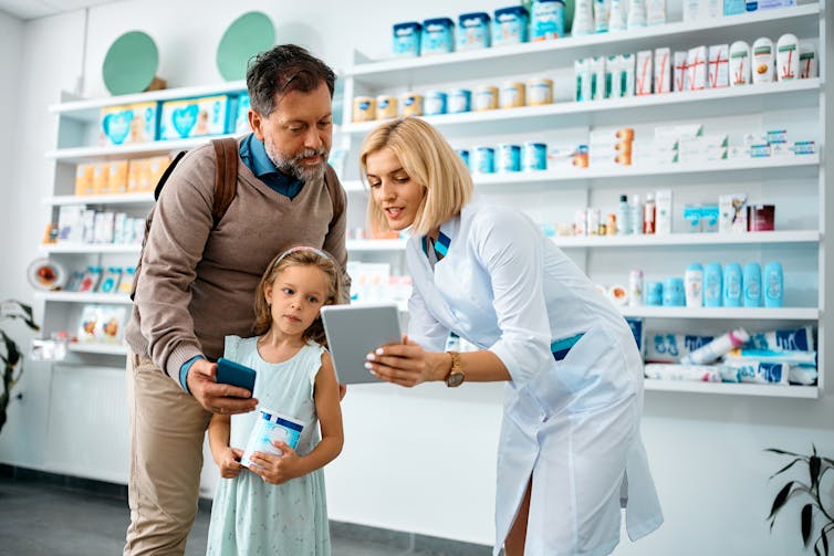 A man, with his daughter, talks to a pharmacist.