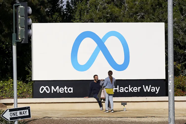 Employees stand outside a large 'Meta' sign at the company's headquarters.