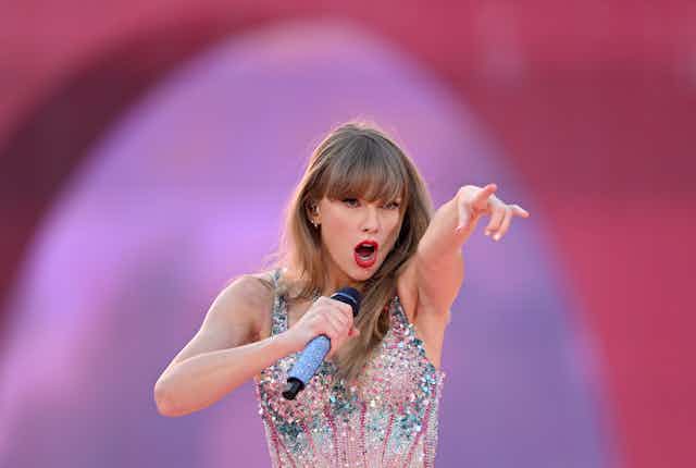 Taylor Swift pointing at the crowd as she performs on stage