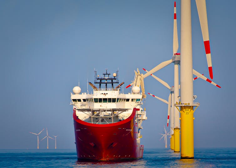 Big red and white boat, next to offshore wind turbines, flat blue sea