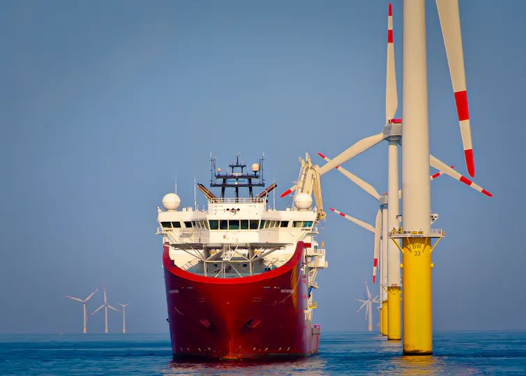 Big red and white boat, next to offshore wind turbines, flat blue sea