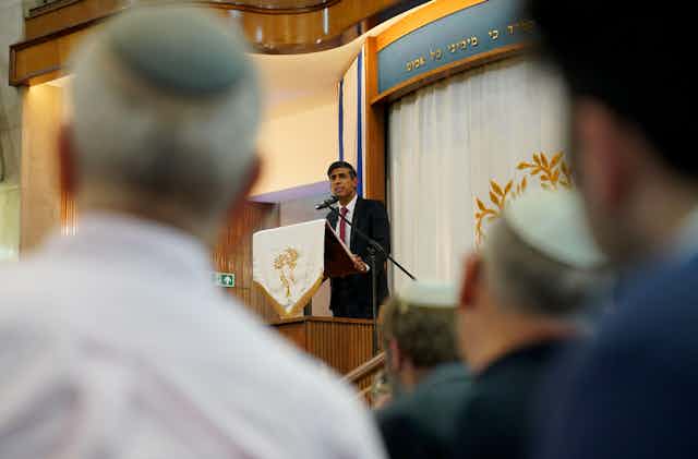 The British prime minister at the lecturn in a synagogue with worshippers in the foreground.