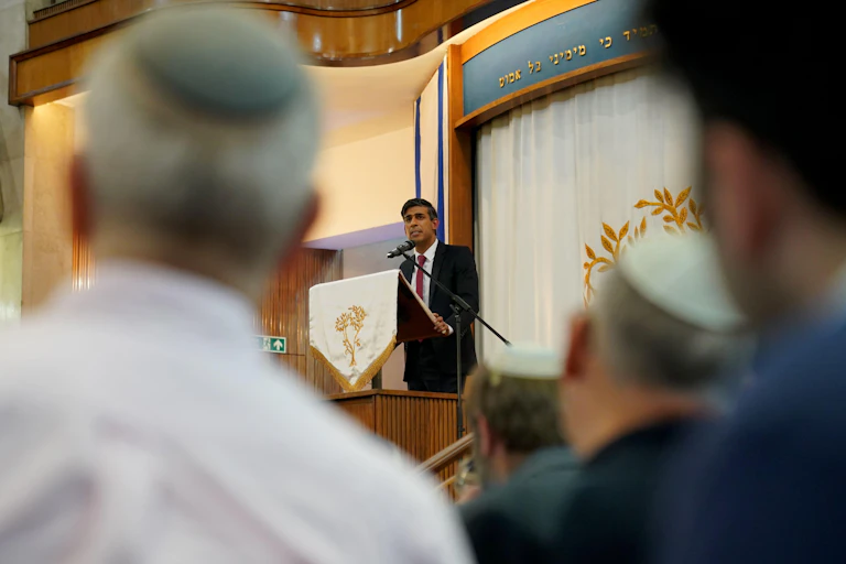 The British prime minister at the lecturn in a synagogue with worshippers in the foreground.