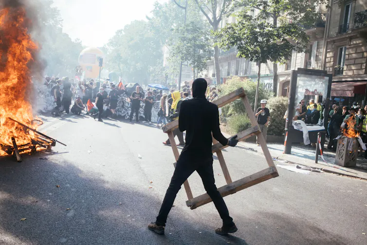 A hooded protester throws objects into a fire during protests against pension reform in France.