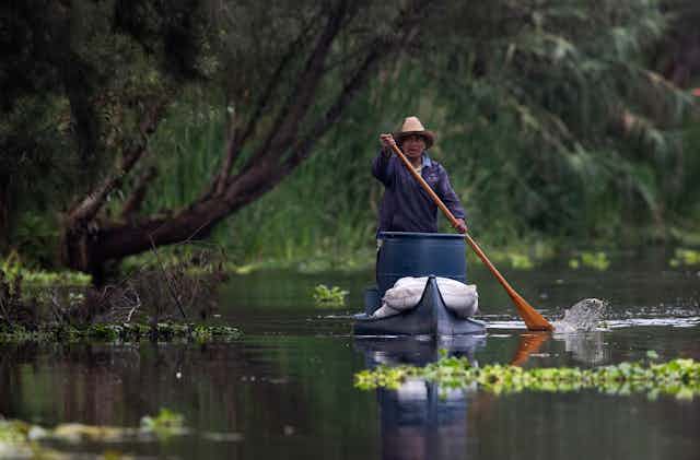 A farmer in a canoe loaded with supplies paddles on a canal.