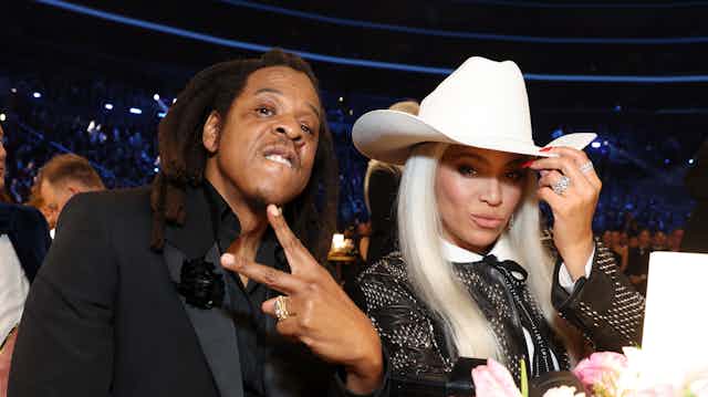 Black woman with long white hair tugs at a white cowboy hat.