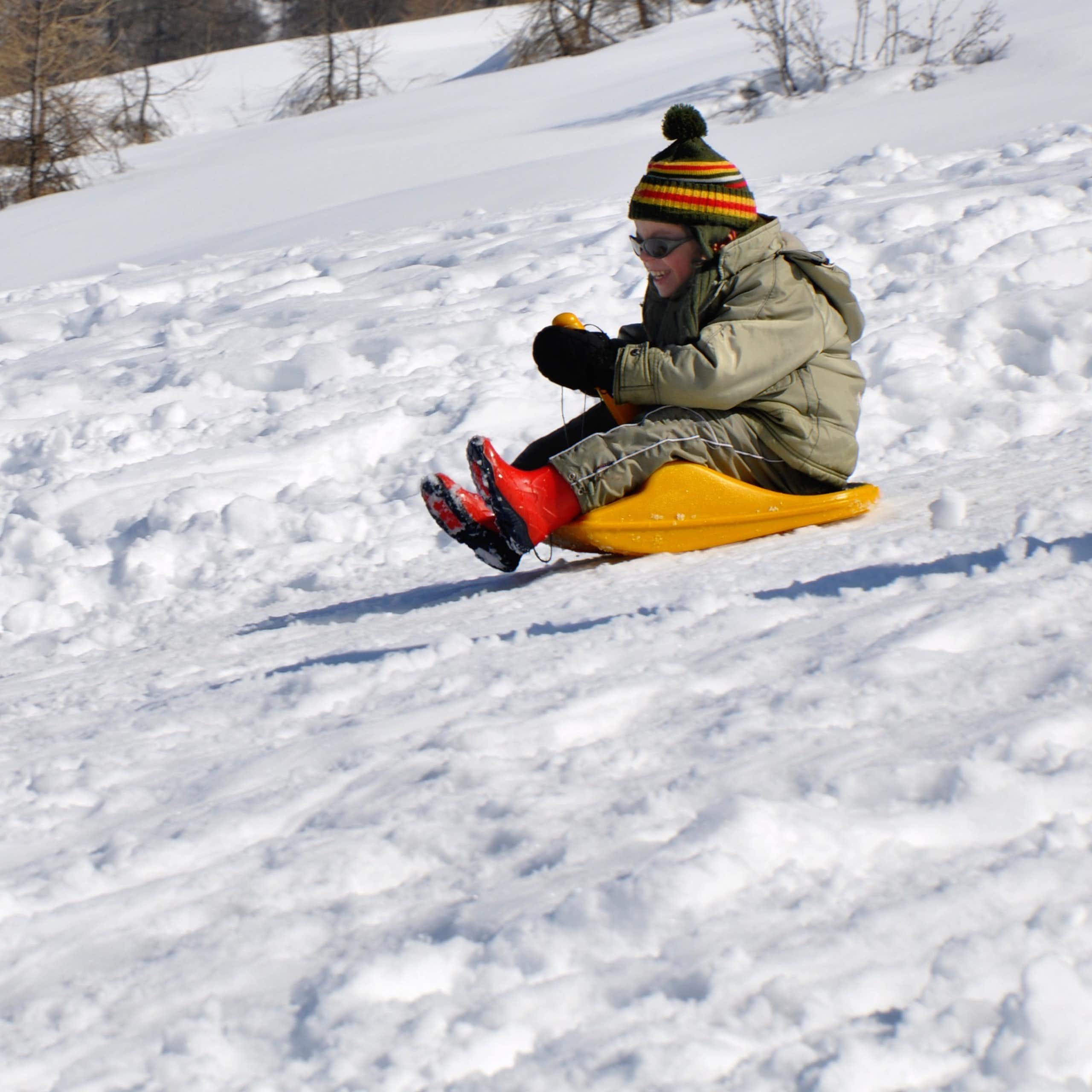 A young girl goes sledding down a snow-covered hill.