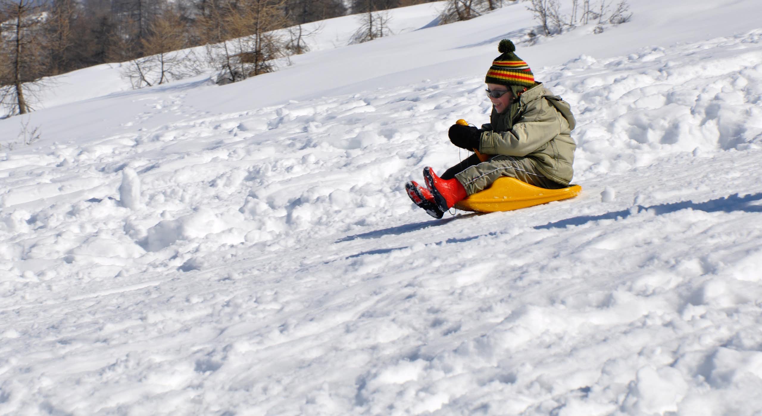 A young girl goes sledding down a snow-covered hill.