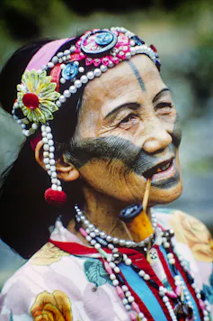 Elderly Taiwanese aboriginal woman smoking a pipe wearing beads headdress.