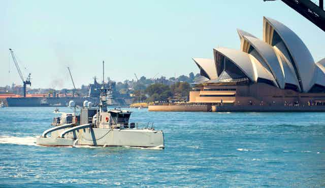 An unscrewed boat sailing through Sydney Harbour, with the Sydney Opera House in the background.