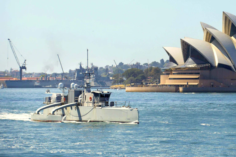 An unscrewed boat sailing through Sydney Harbour, with the Sydney Opera House in the background.