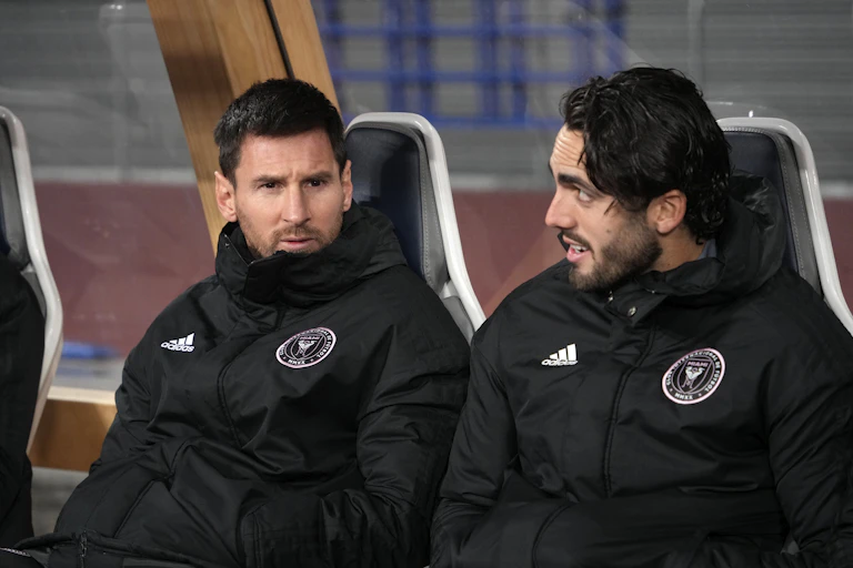 Lionel Messi sat on a chair in a dugout next to a teammate.