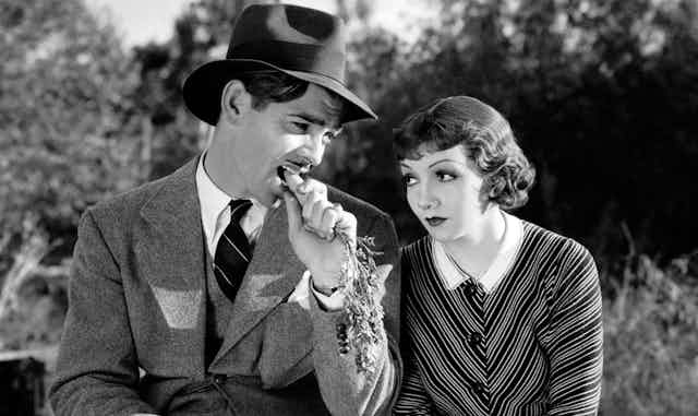Clark Gable bites a carrot while Claudette Colbert looks on in disdain. 