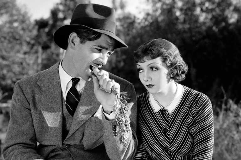 Clark Gable bites a carrot while Claudette Colbert looks on in disdain.