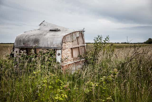 A derelict, abandoned caravan in a rural field, against a grey sky