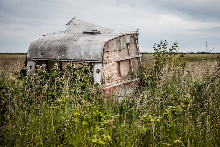 A derelict, abandoned caravan in a rural field, against a grey sky
