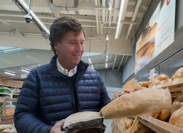 A man in a navy blue puff jacket, holding loaves of bread in a grocery store.