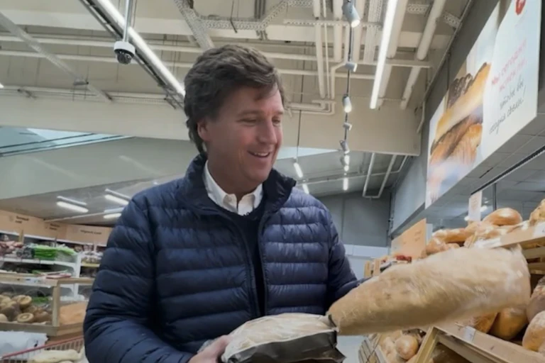 A man in a navy blue puff jacket, holding loaves of bread in a grocery store.