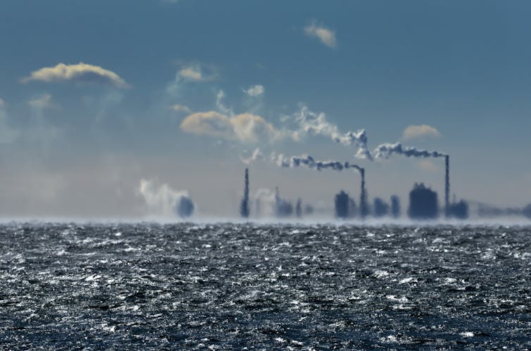 Hazy smoke stacks are seen in the distance with water in the foreground.
