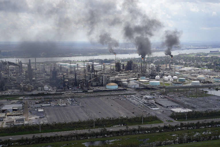 Smoke and smokestacks seen in an industrial plant alongside a river.