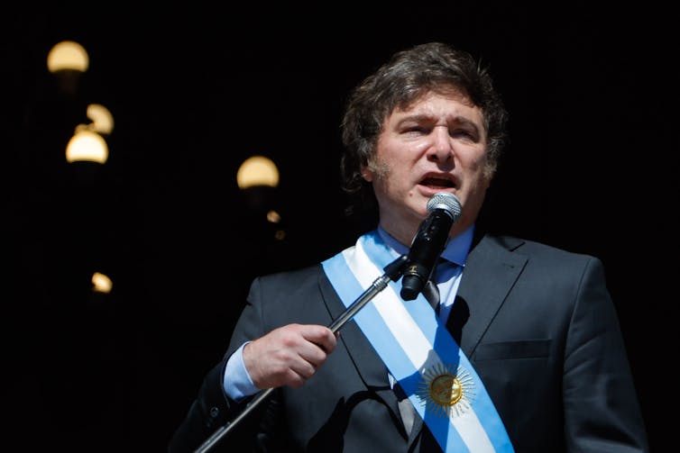 Argentina's president, Javier Milei, draped in the Argentinian flag and speaking into a microphone.