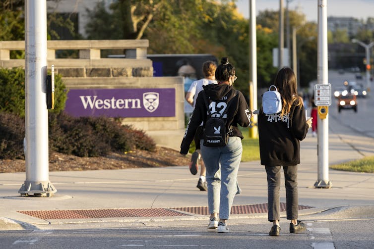 Two students cross a street in front of a sign that says 'Western'