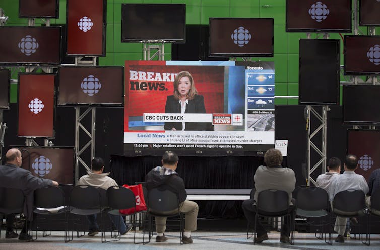 people in chairs watching CBC news on a large screen surrounded by others displaying the CBC logo.