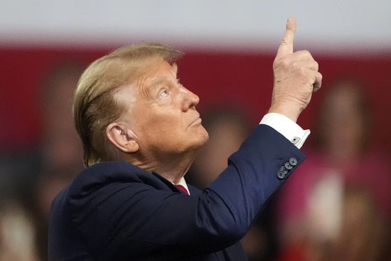 A rotund man with blond-grey hair points up.