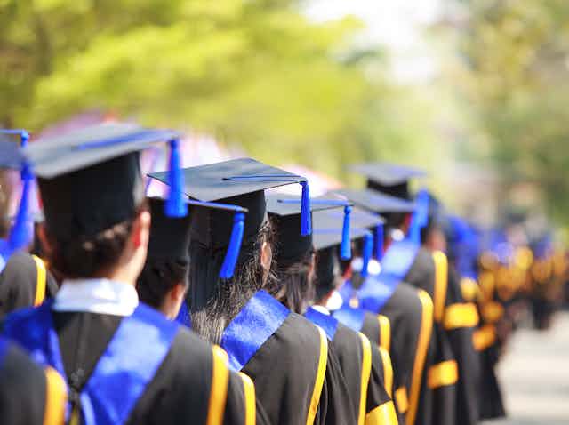 A line of students in graduation gowns and caps waiting outside